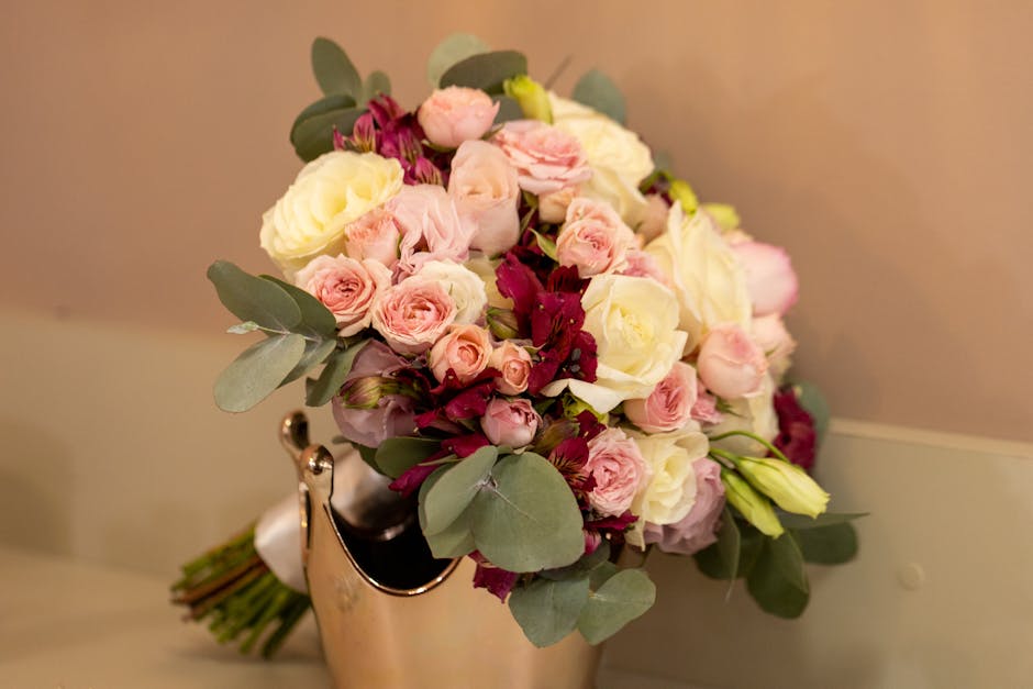 A floral bouquet featuring a mix of fresh, pastel-colored flowers including soft pink roses, creamy white roses, and light pink spray roses, arranged with green eucalyptus leaves. The bouquet is place